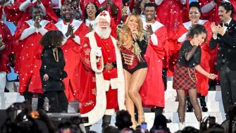 Mariah Carey performs during a holiday event surrounded by a choir and Santa Claus.