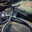 A stethoscope, military dog tags, and a first aid kit on a camouflage background. A stethoscope, military dog tags, and a first aid kit on a camouflage background.