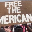 A crowd holding a sign that reads "FREE THE AMERICANS." A crowd holding a sign that reads "FREE THE AMERICANS."