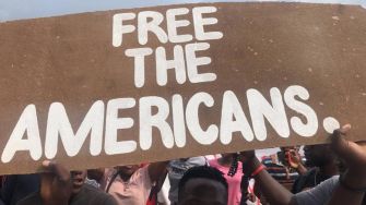A crowd holding a sign that reads "FREE THE AMERICANS."