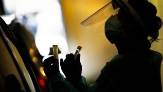 A healthcare worker in personal protective equipment holding test tubes while performing a COVID-19 test.