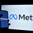A person holding a smartphone displaying the Facebook logo in front of a screen with the Meta logo. A person holding a smartphone displaying the Facebook logo in front of a screen with the Meta logo.