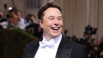 Elon Musk smiling at a public event, wearing a tuxedo with a bow tie.