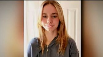 Portrait of a teenage girl with long, light brown hair, wearing a grey zip-up hoodie.