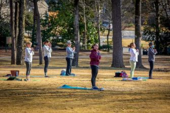 Groups of people practicing yoga outdoors on mats in a park.