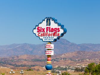 Sign for Six Flags California featuring attractions and a gift shop, set against a mountainous backdrop.