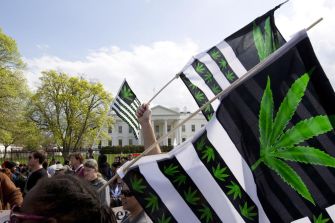 Protesters holding flags with marijuana leaf designs in front of the White House during a demonstration following President Biden's announcement on pardoning individuals convicted of marijuana possession.