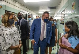 Group of people wearing masks in a school hallway, engaged in discussion with a child.