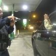 A police officer points a gun at a man with his hands raised inside a car during a traffic stop at a gas station. A police officer points a gun at a man with his hands raised inside a car during a traffic stop at a gas station.