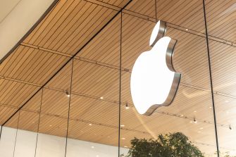Apple logo on the exterior of an Apple Store, featuring a modern design with wooden ceiling and glass reflections.