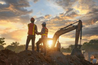 Construction workers discussing a project at sunset, with heavy machinery in the background.