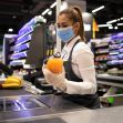 A cashier wearing a mask and gloves scans groceries at a checkout counter in a store. A cashier wearing a mask and gloves scans groceries at a checkout counter in a store.