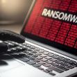 A hand wearing a black glove on a laptop keyboard, with a screen displaying the word "RANSOMWARE" in bold letters against a red background. A hand wearing a black glove on a laptop keyboard, with a screen displaying the word "RANSOMWARE" in bold letters against a red background.