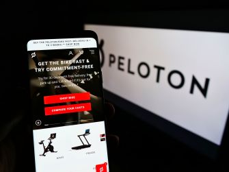 A phone displaying the Peloton website in front of a Peloton logo.