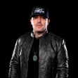 Image of a man wearing a black leather jacket and a cap, against a dark background. Image of a man wearing a black leather jacket and a cap, against a dark background.