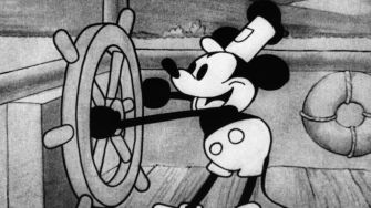 Black and white image of Mickey Mouse in "Steamboat Willie," steering a ship's wheel.