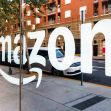 Amazon logo displayed on a storefront window with a city street view in the background. Amazon logo displayed on a storefront window with a city street view in the background.