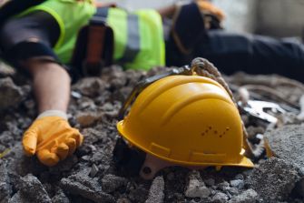 Construction helmet on rubble with an injured worker in the background.