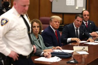 Donald Trump seated at a courtroom table during an indictment hearing, accompanied by legal representatives and court personnel.