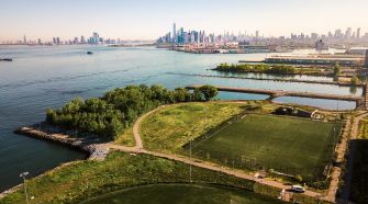 A crowd at a rally supporting the "Touch Grass" bill, advocating for natural grass in NYC parks, with signs addressing concerns about synthetic turf.