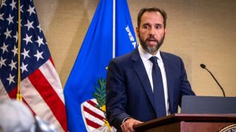 Special Counsel Jack Smith speaking at a press conference regarding the indictment against Donald Trump, with flags in the background.