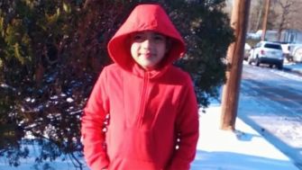 A young boy wearing a red hoodie standing outdoors in a snowy landscape.