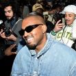 Kanye West surrounded by fans and photographers, smiling while wearing sunglasses and a denim jacket. Kanye West surrounded by fans and photographers, smiling while wearing sunglasses and a denim jacket.