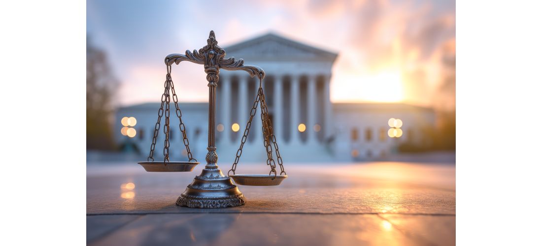 A scale of justice in front of the U.S. Supreme Court building at sunset.