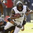 A college football player running with the ball while being tackled during a game. A college football player running with the ball while being tackled during a game.