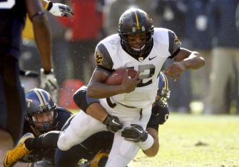 A college football player running with the ball while being tackled during a game.
