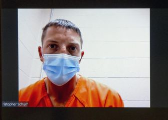 Police officer Christopher Schurr appearing in court via video link, wearing an orange jumpsuit and a mask.