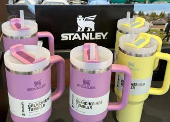 A display of colorful Stanley Quencher tumblers in various sizes, with a logo prominently featured in the background.