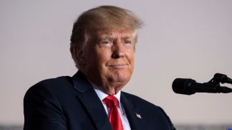 Former President Donald Trump speaking at an event, wearing a suit and a red tie.