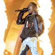 Travis Scott performing on stage with flames in the background during a concert. Travis Scott performing on stage with flames in the background during a concert.
