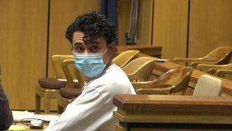 A man in a courtroom wearing a face mask, facing the camera.