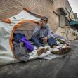 A person sitting in front of a tent in an urban environment, surrounded by belongings. A person sitting in front of a tent in an urban environment, surrounded by belongings.