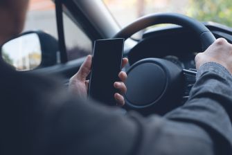 A driver holding a smartphone while gripping the steering wheel of a car.