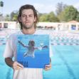 Man holding a vinyl record of Nirvana's "Nevermind" album in front of a swimming pool. Man holding a vinyl record of Nirvana's "Nevermind" album in front of a swimming pool.