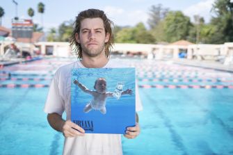 Man holding a vinyl record of Nirvana's "Nevermind" album in front of a swimming pool.