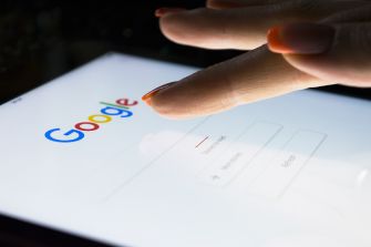 A close-up of a finger poised over the Google search page on a tablet, highlighting Google's search interface.