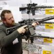 A person examining a modern firearm in a display featuring various rifles. A person examining a modern firearm in a display featuring various rifles.