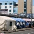 Tents set up along a city street, indicating a homeless encampment surrounded by urban buildings. Tents set up along a city street, indicating a homeless encampment surrounded by urban buildings.