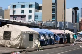 Tents set up along a city street, indicating a homeless encampment surrounded by urban buildings.