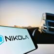 Image of a smartphone displaying the Nikola Motors logo, with a blurred image of a truck on a road in the background. Image of a smartphone displaying the Nikola Motors logo, with a blurred image of a truck on a road in the background.