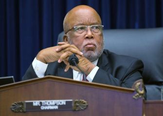 A man with glasses and a serious expression sits at a desk labeled "Chairman."