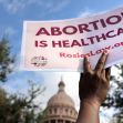 A person holding a sign that reads "ABORTION IS HEALTHCARE" in front of a Texas state building. A person holding a sign that reads "ABORTION IS HEALTHCARE" in front of a Texas state building.