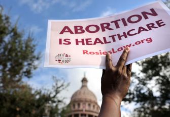 A person holding a sign that reads "ABORTION IS HEALTHCARE" in front of a Texas state building.