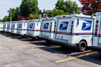 Row of U.S. Postal Service delivery trucks parked in a lot.