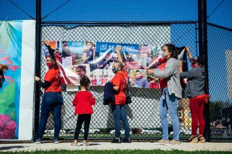 A group of people in red outfits are hanging a banner on a fence, advocating for the rights of undocumented immigrants.