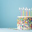 A colorful birthday cake with lit candles and vibrant sprinkles against a light blue background. A colorful birthday cake with lit candles and vibrant sprinkles against a light blue background.